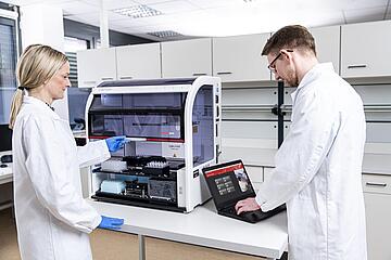 two people setting up a CyBio Felix liquid handler with microplates and software