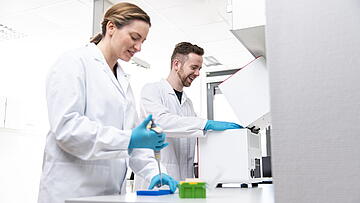 Two persons in a lab, pipetting