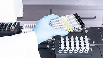 a gloved hand placing labware on the deck of a Felix liquid handler for setting up a Jess automated western blot run