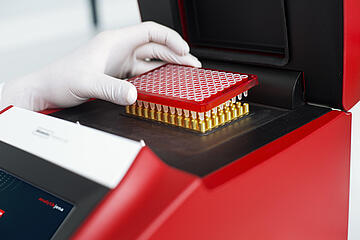 a gloved hand placing a 96-well PCR plate into a Biometra TAdvanced thermal cycler
